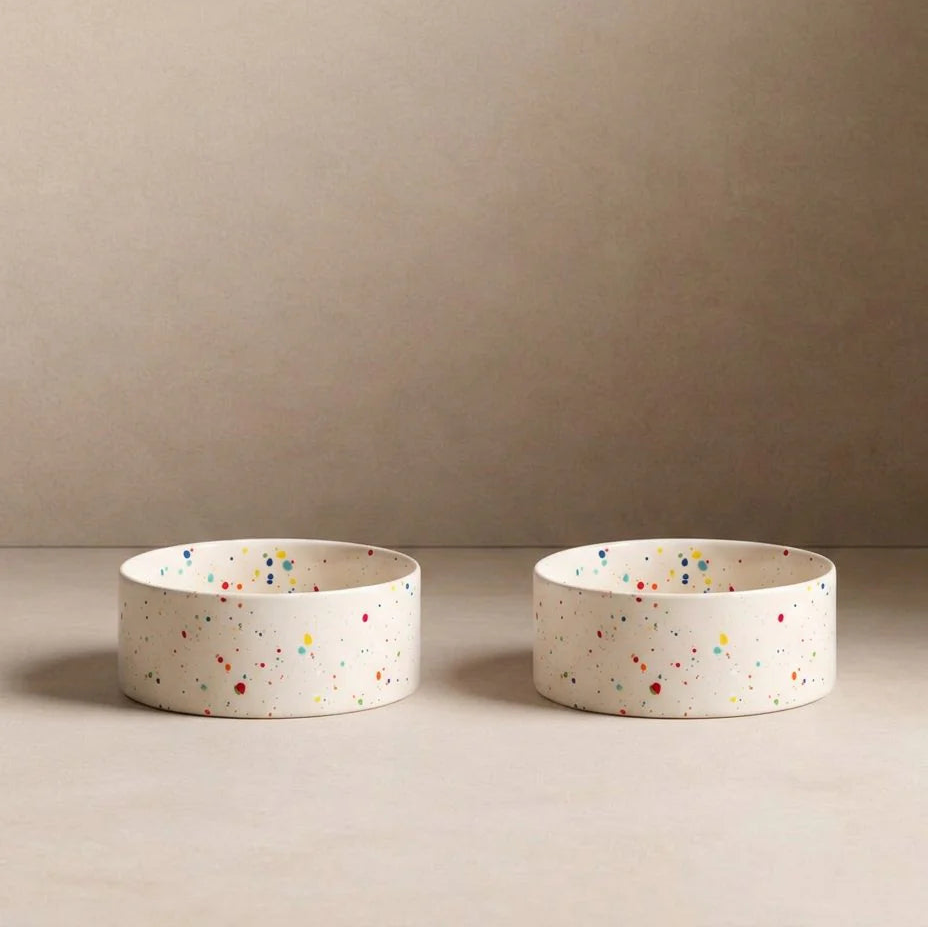 Two ceramic pet bowls with speckled patterns on a beige background