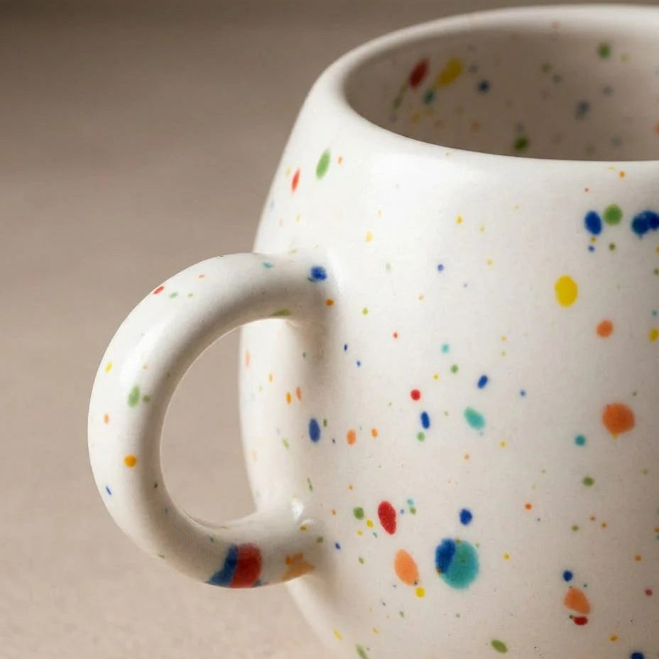White mug with colorful speckles on a beige background